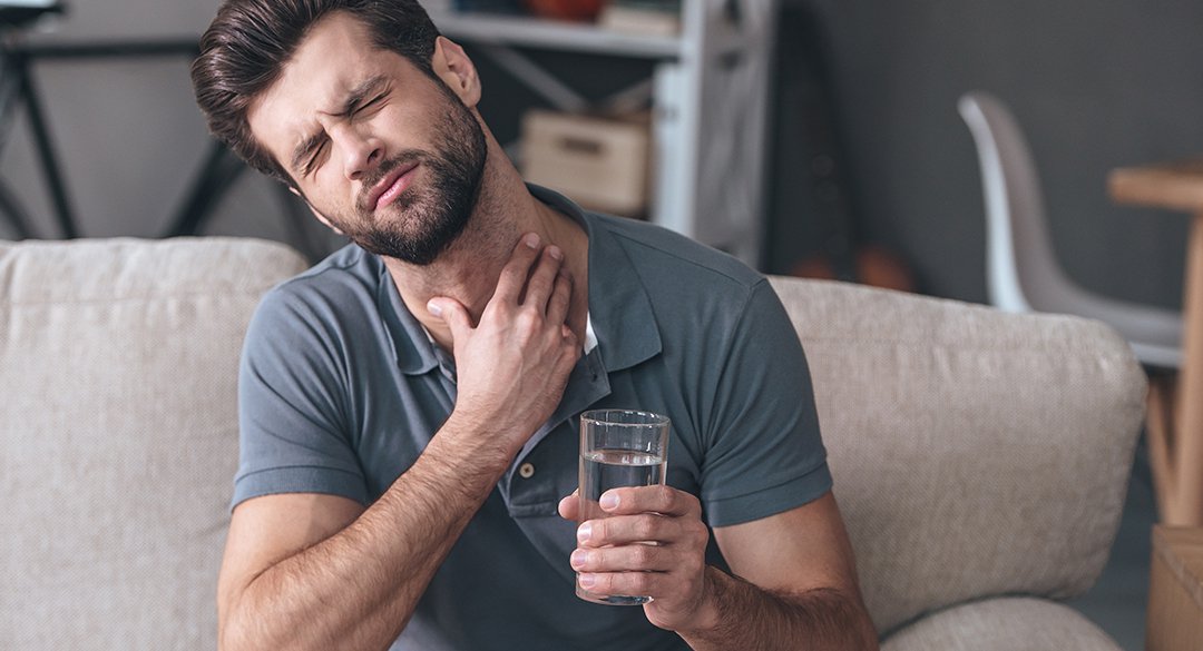 Man with a sore throat drinking a glass of water