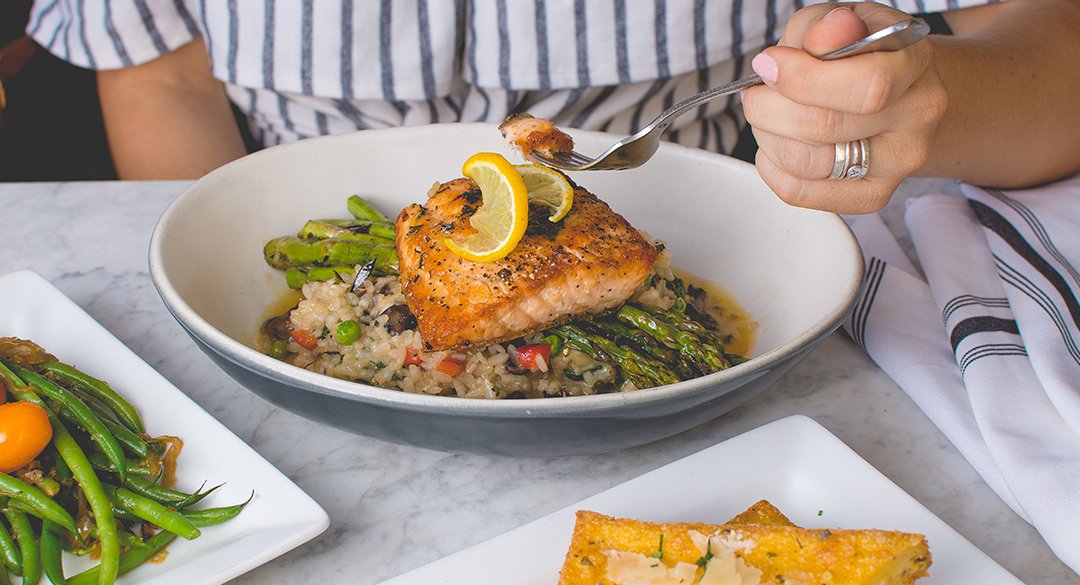 Person holding fork eating a plate of salmon