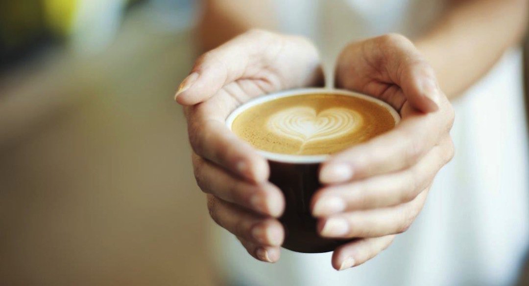 Person holding a cup of coffee with heart shaped foam