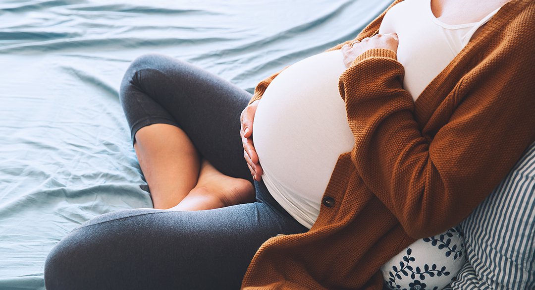 Woman holding pregnant stomach and sitting on bed