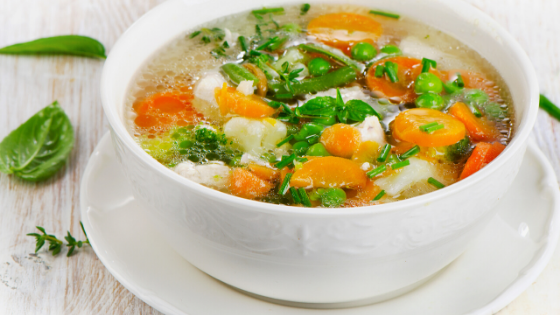 A bowl of hot chicken soup sits on a table-6.png