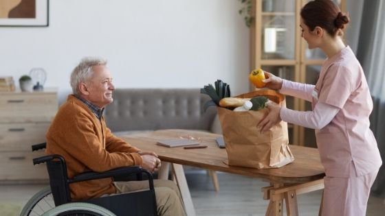 A female caregiver bings in groceries for a senior man in a wheelchair-1.jpeg
