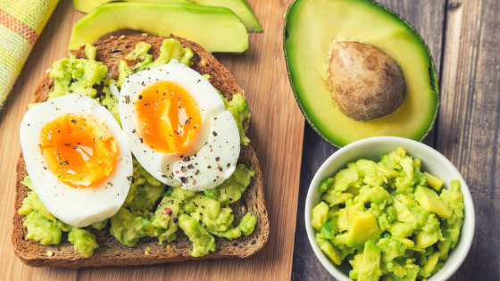 A halved avocado sits next to a plate of avocado toast and a bowl of guacamole-6.png