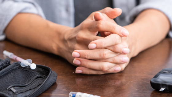 A person's hands are seen clasped with diabetes treatment & monitoring equipment around them-1.png