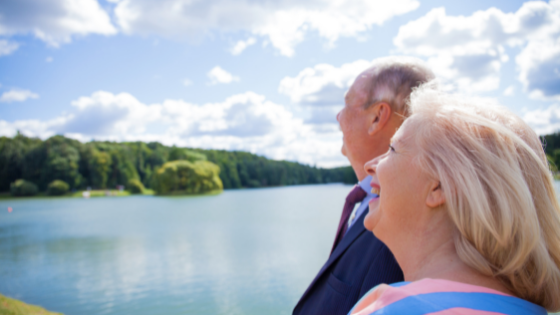 A senior couple stands at a lake and looks up at the clouds-2.png