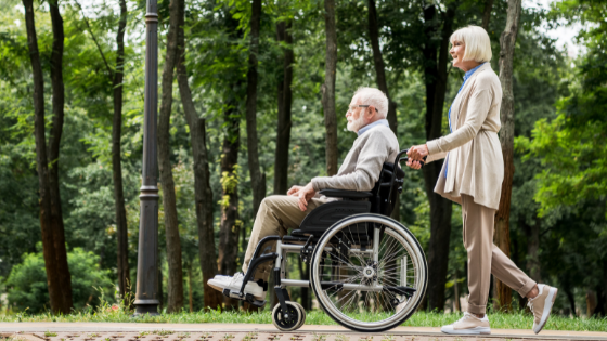 A senior man in a wheelchair and his wife take a stroll through a wooded trail-1.png