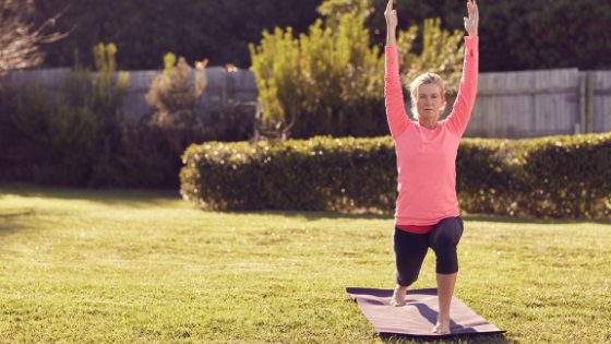A senior woman is seen in Warrior I pose on her yoga mat in the backyard-5.png