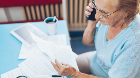 A senior woman looks at paperwork while on the phone-7.png