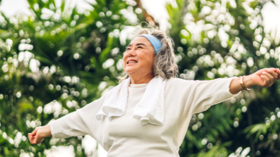 A senior woman smiles as she stretches her arms outward while outdoors-1.png