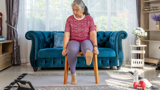 A senior woman watching an exercise video in her living room stretches her foot-3.png
