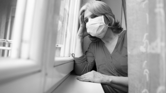 A senior woman wearing a mask is seen looking longingly out of a window-1.png