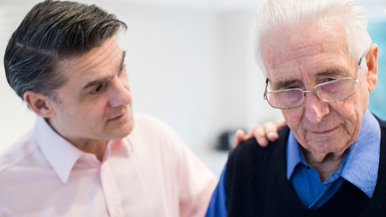 An adult male comforts an confused looking older man with glasses-5.png