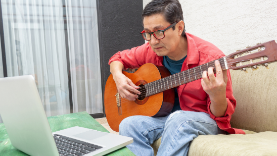 An older man is seen learning to play the guitar by computer-5.png