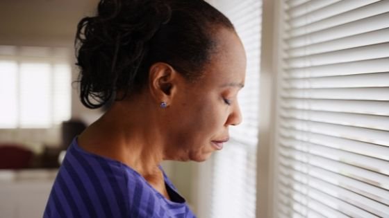 An older senior woman looks sad though blinds-6.jpeg