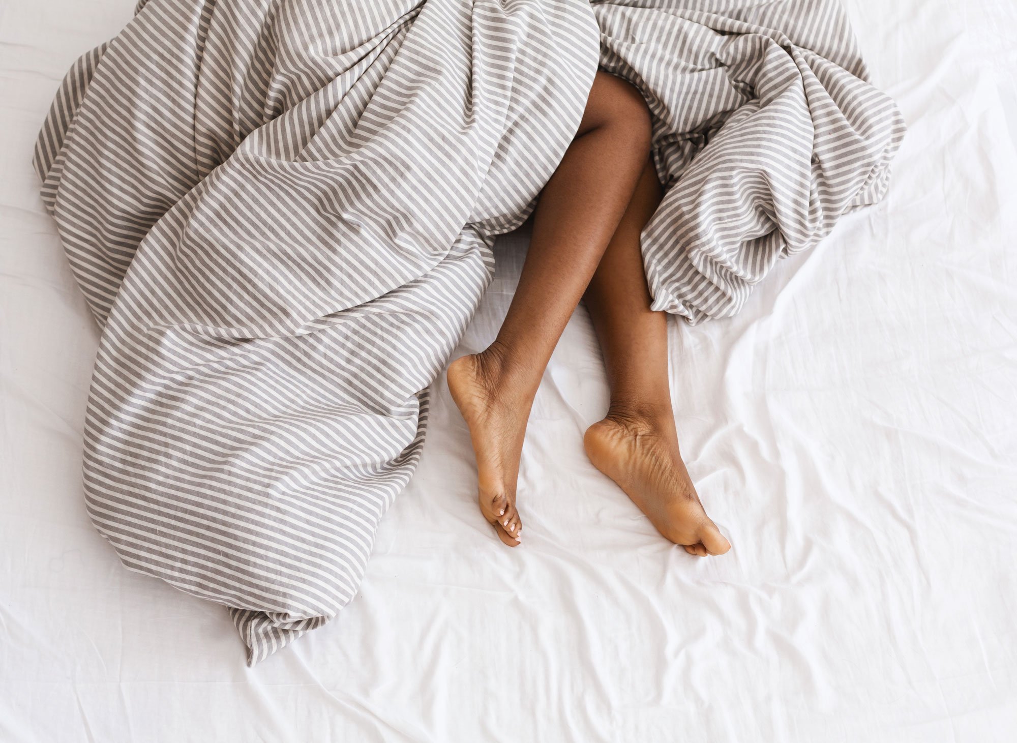 Woman's legs sticking out of sheets on bed