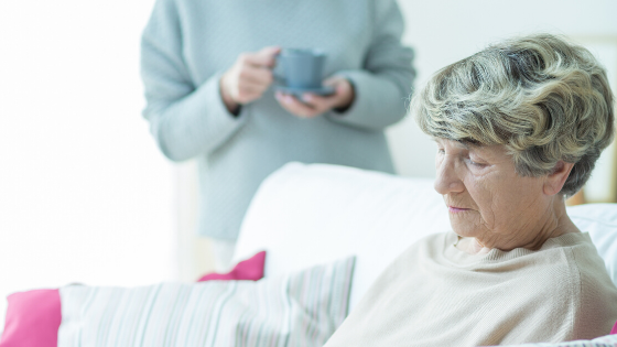 Older woman sits on couch looking upset while another woman stands holding a cup of coffee in the background-8.png