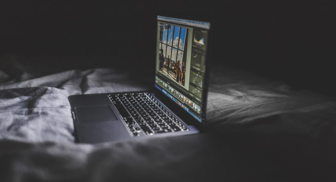 Laptop open on a bed in a dark room