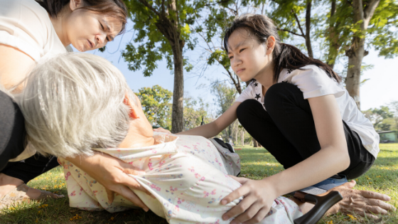 Two younger Asian women attend to an elder woman who has fainted in the park-2.png