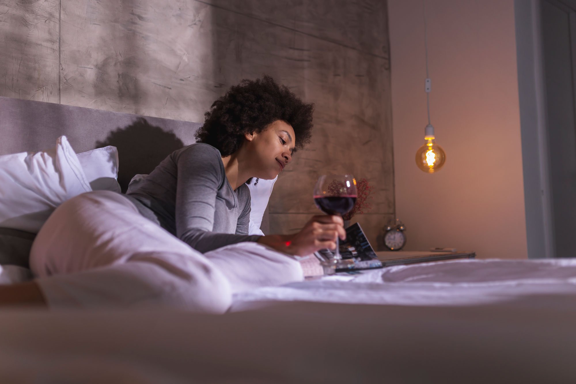 Woman reading a magazine and drinking wine in bed