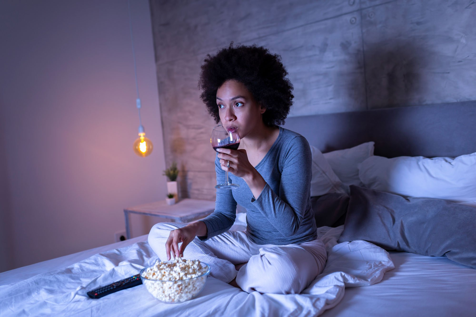 Woman drinking wine and eating popcorn in bed