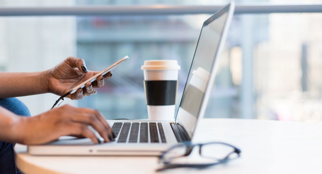 Hands holding mobile device and typing on laptop