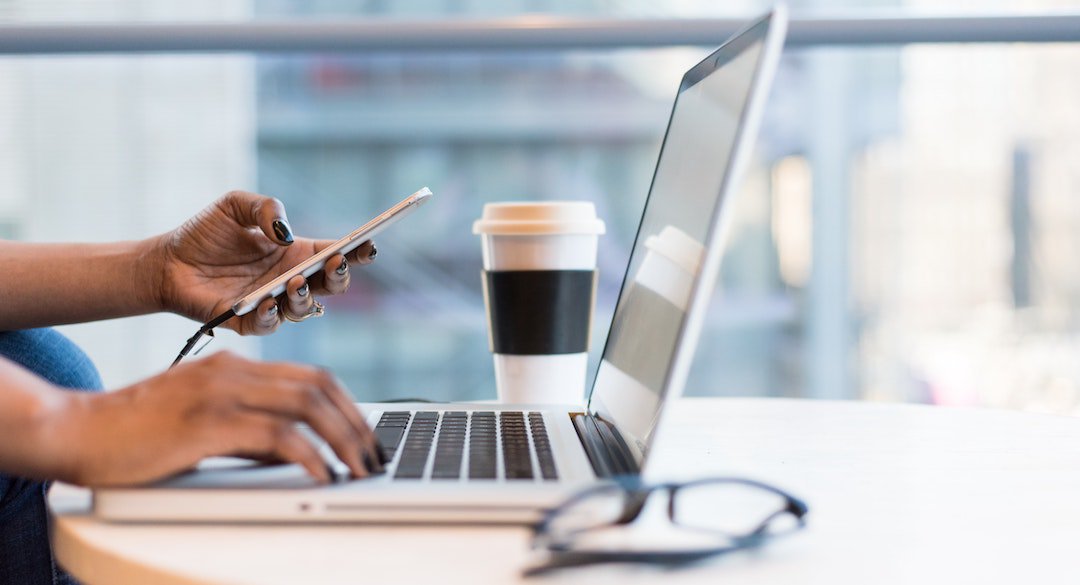 Hands holding mobile device and typing on laptop