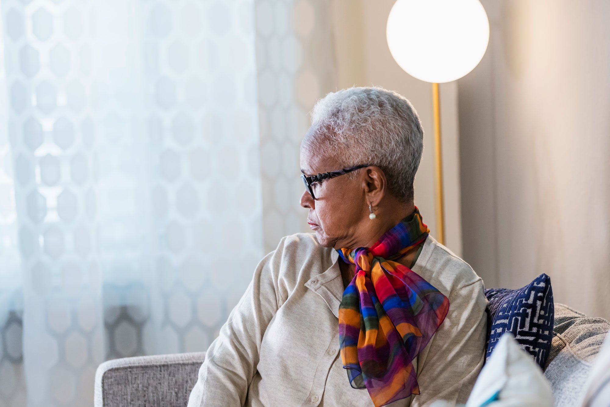 Woman sitting on couch looking out window with a serious expression