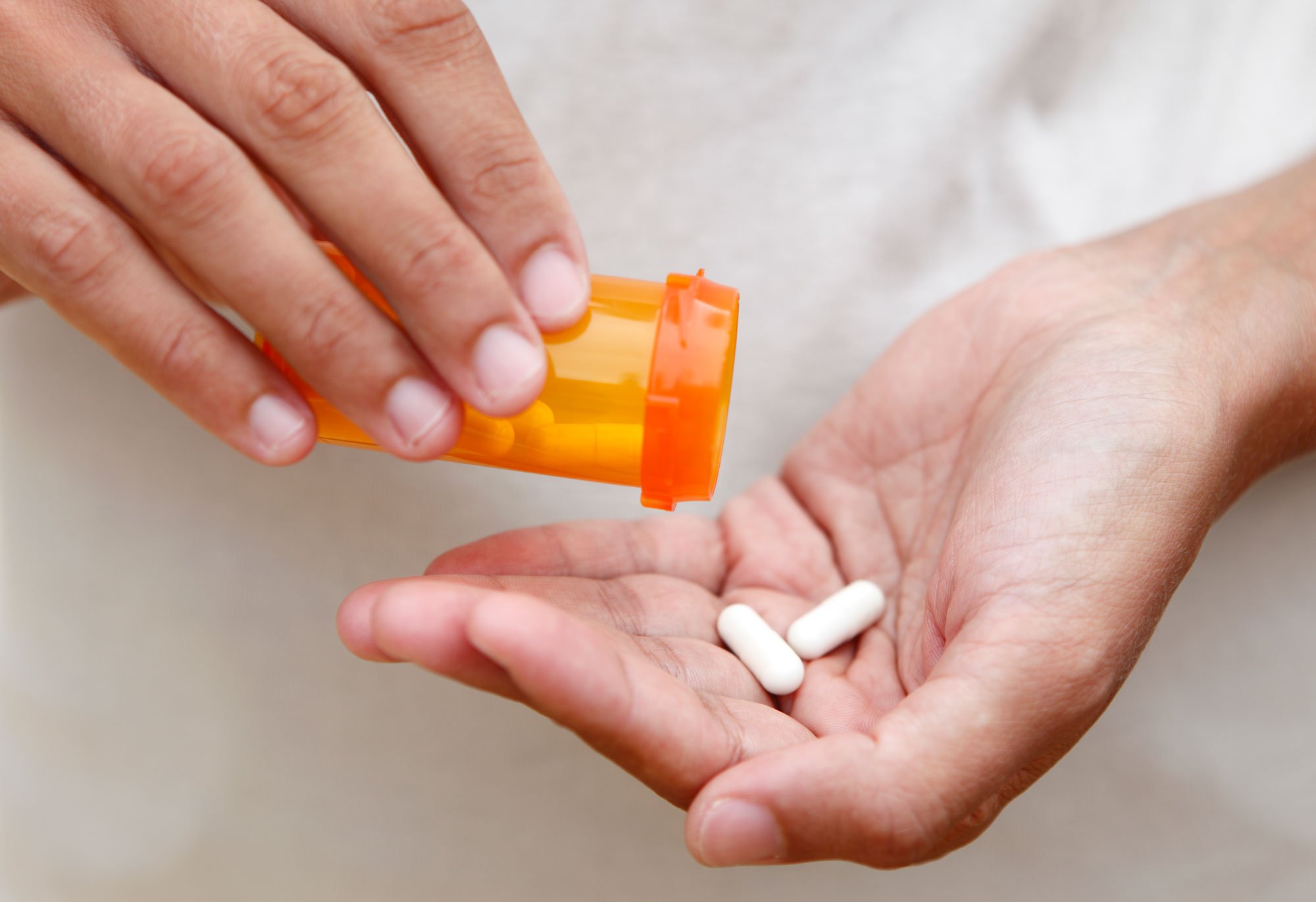 Close up of woman holding two pills and pill bottle in her hands