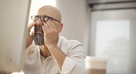 Man rubbing his eyes in front of a computer monitor