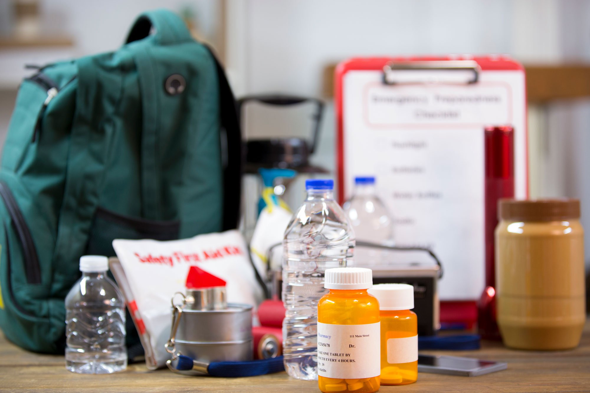 A photo of a collection of emergency supplies including water bottles, a flashlight, a backpack, medicine bottles, etc.
