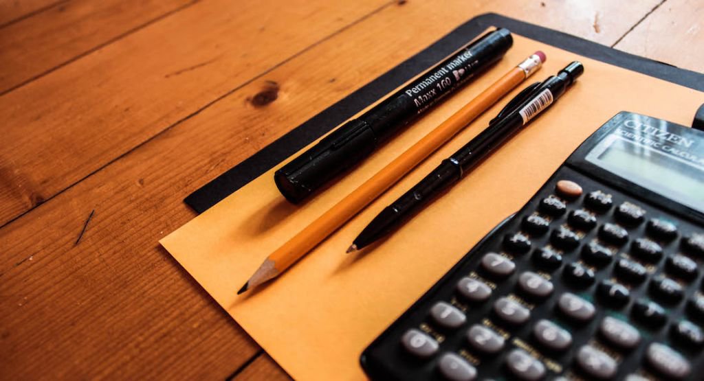 Close up of pencil and pens next to a calculator