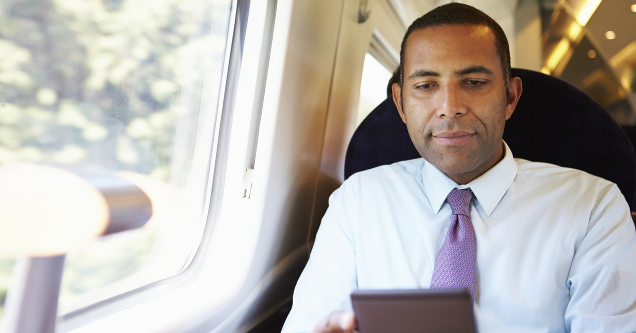Man in a tie sitting on a train and reading on a tablet