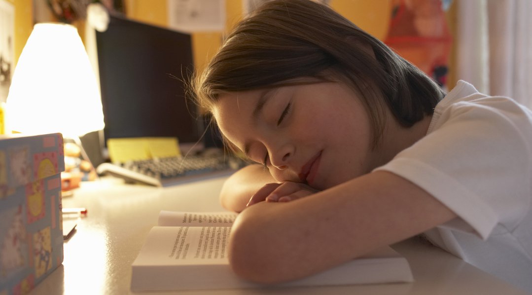 Girl (6-8) resting head on book, eyes closed, close-up