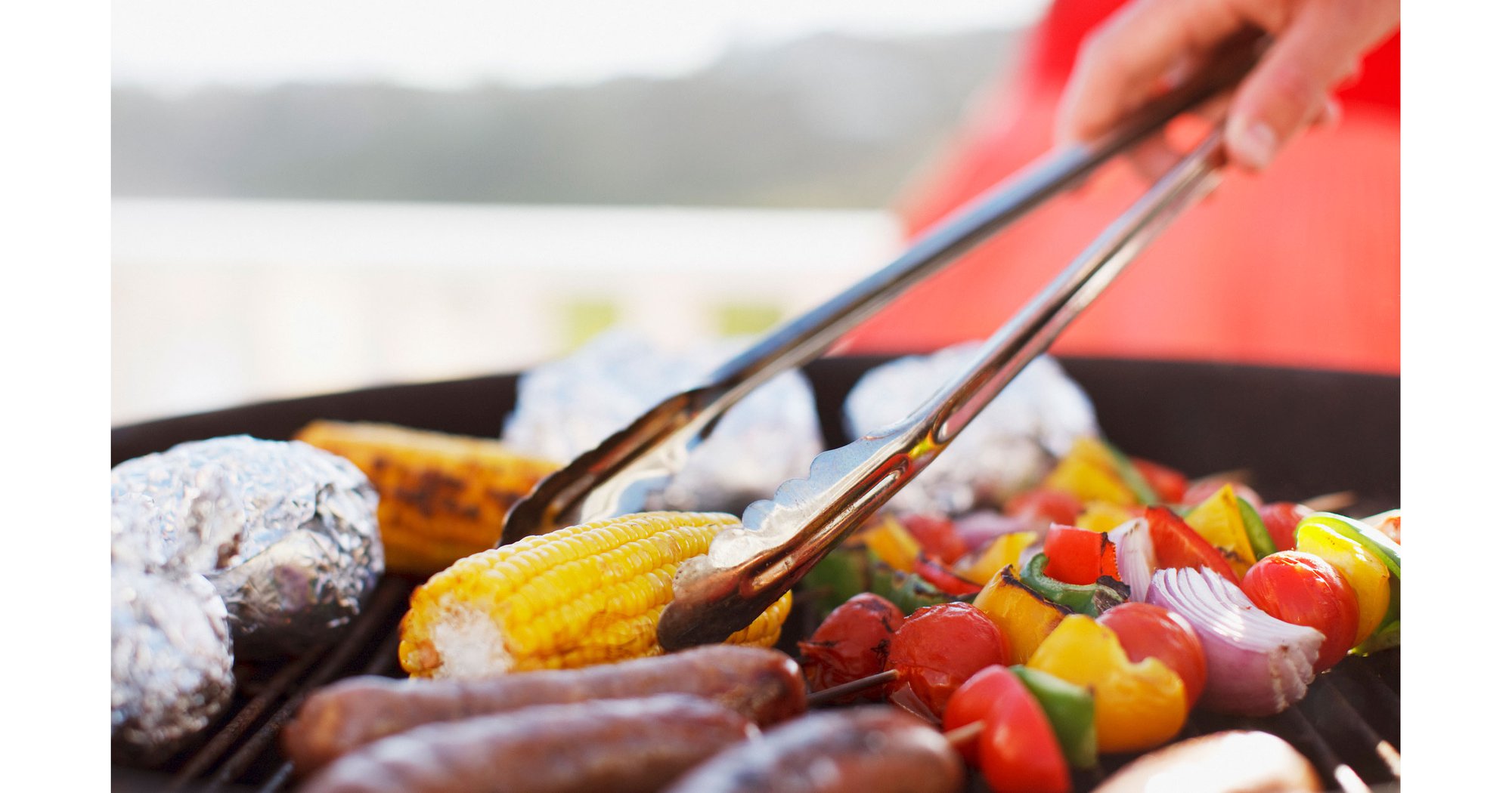 Close up of man using tongs to move food on grill