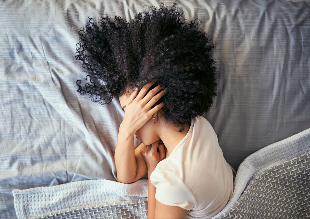 Woman laying on side in bed covering her face with her hand.