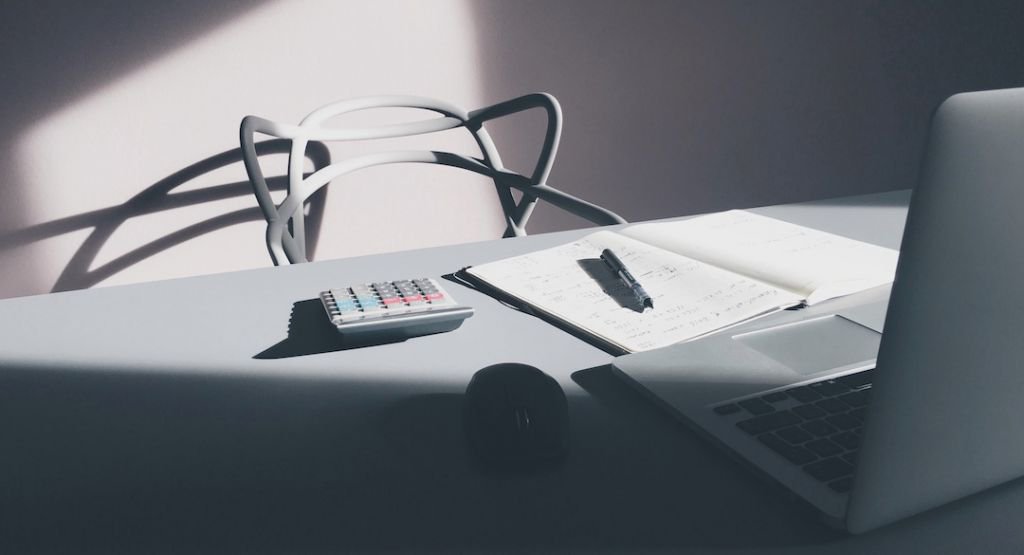 Calculator pen and paper on desk in front of laptop