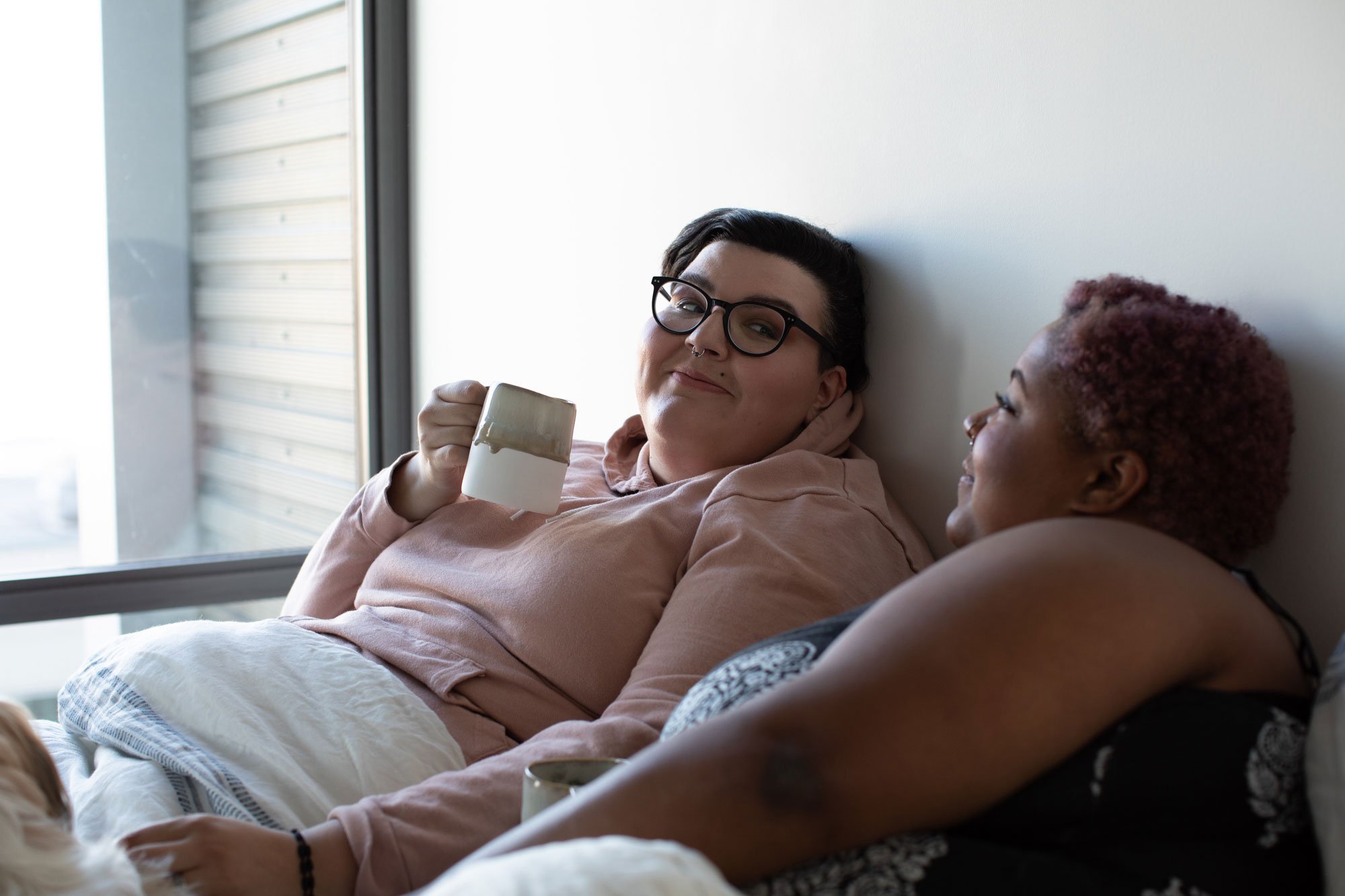 Two women sitting in bed drinking coffee
