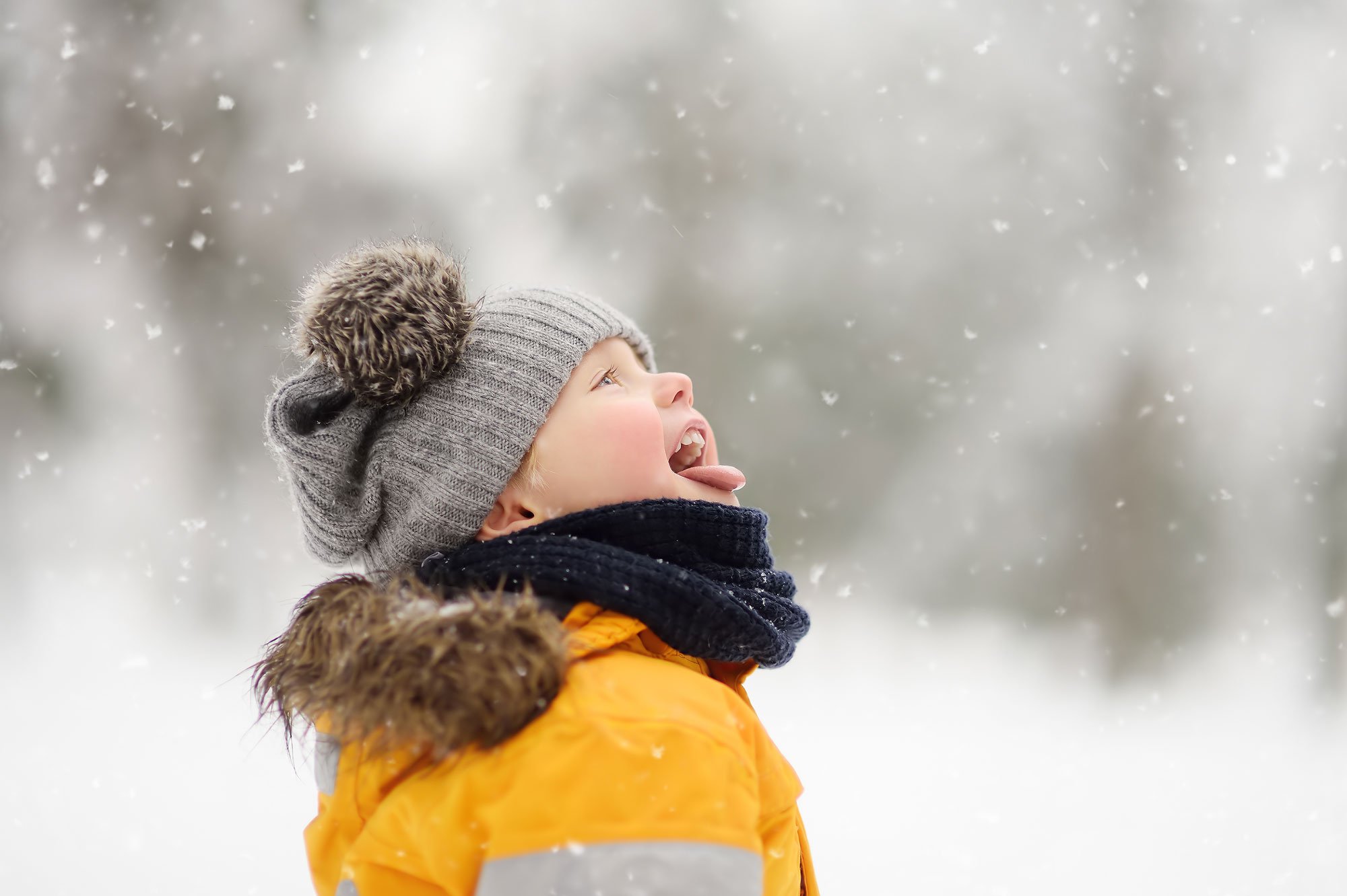 menino baixo com neve em casaco amarelo e chapéu de lã