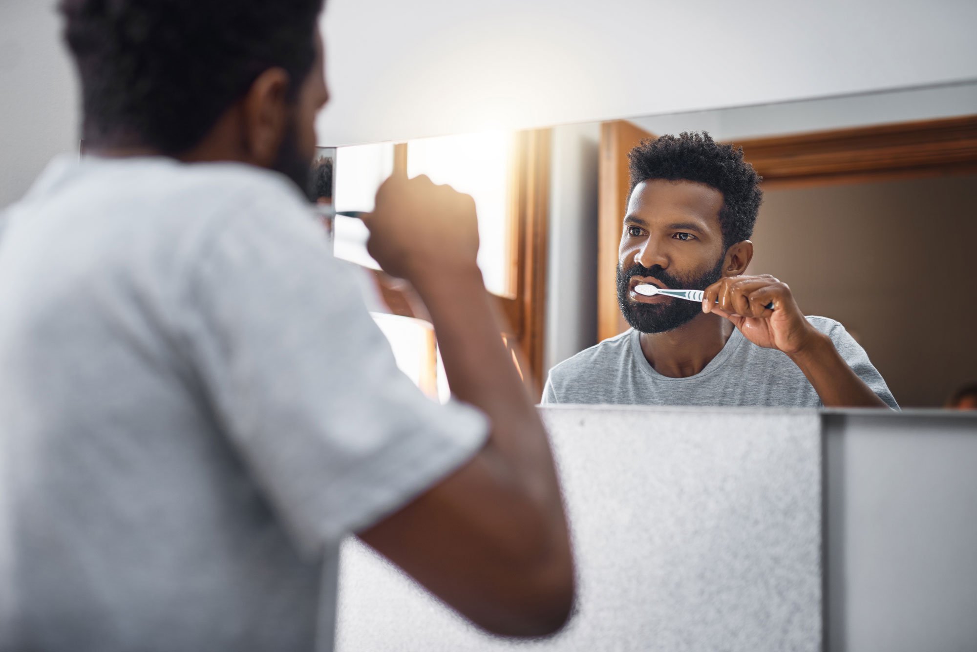 Man watching himself brush his teeth in the mirror