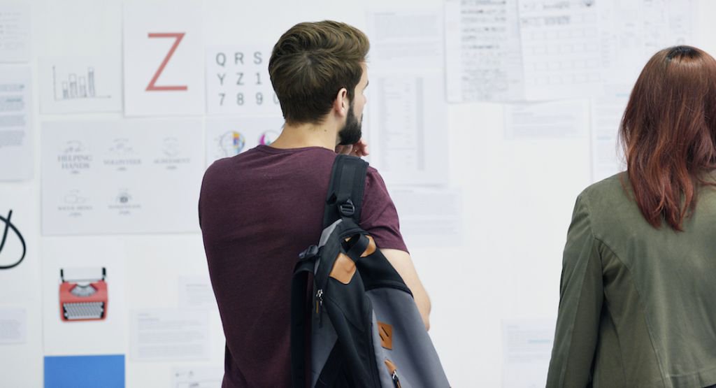 Man holding backpack and woman looking at wall of documents