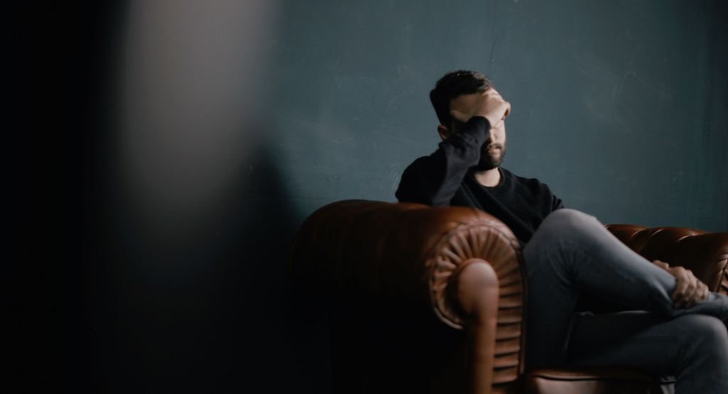 Man sitting on sofa holding his head