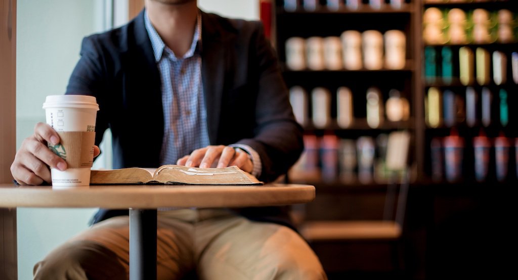 Close up of man reading a book holding a cup of coffee