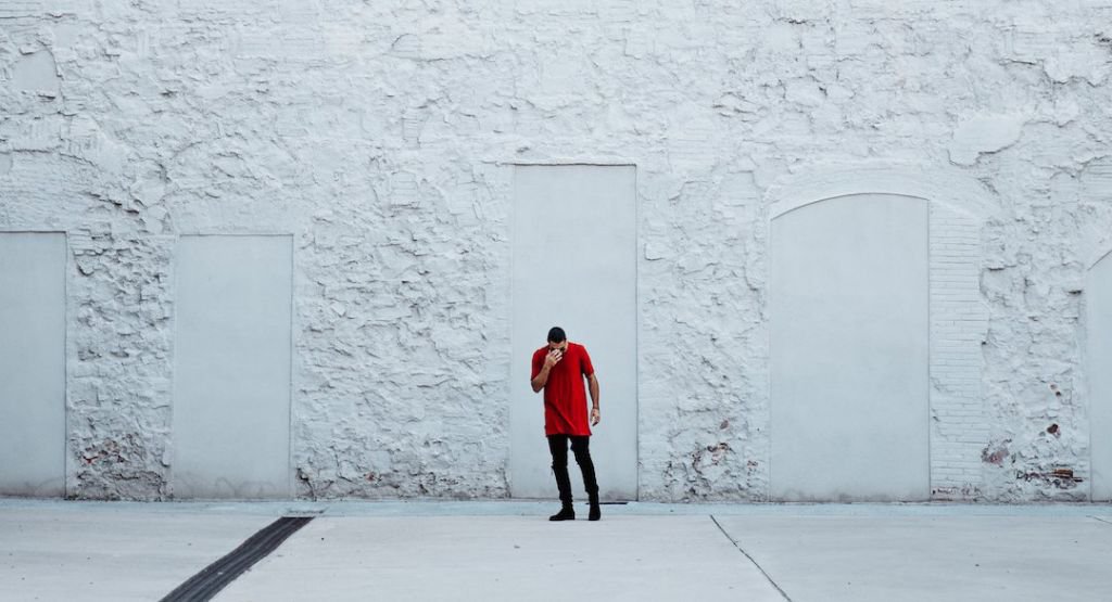 Man standing in front of white wall holding his head