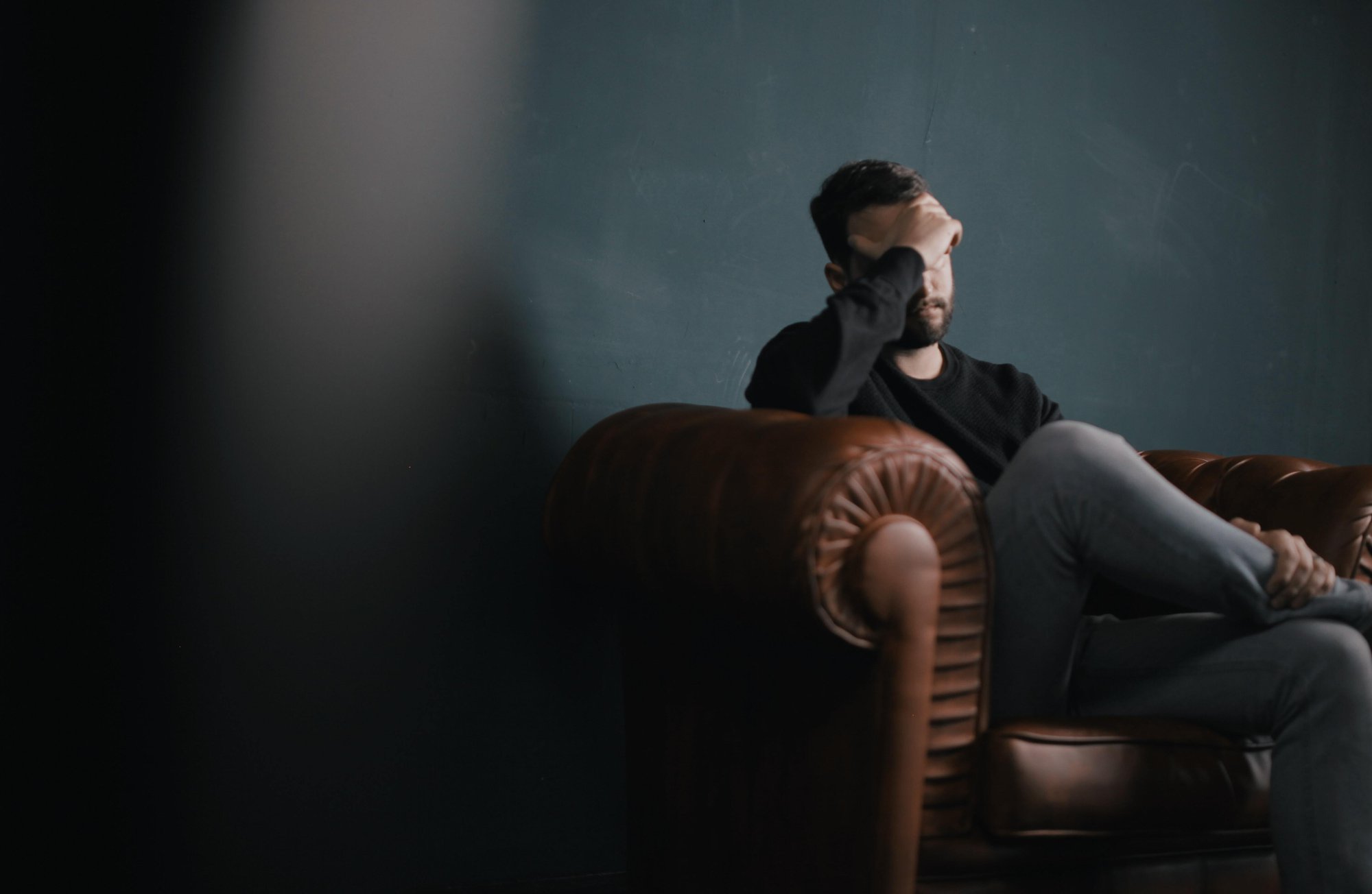 Man sitting in chair with hand on his forehead