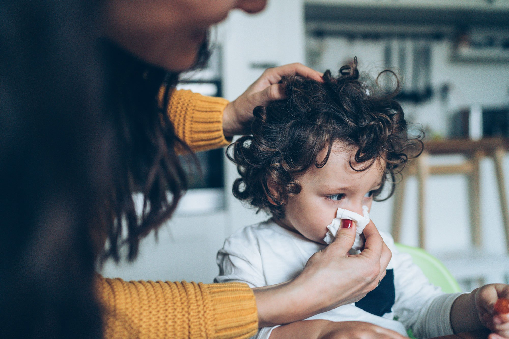 Mother helping young son blow his nose into a tissue