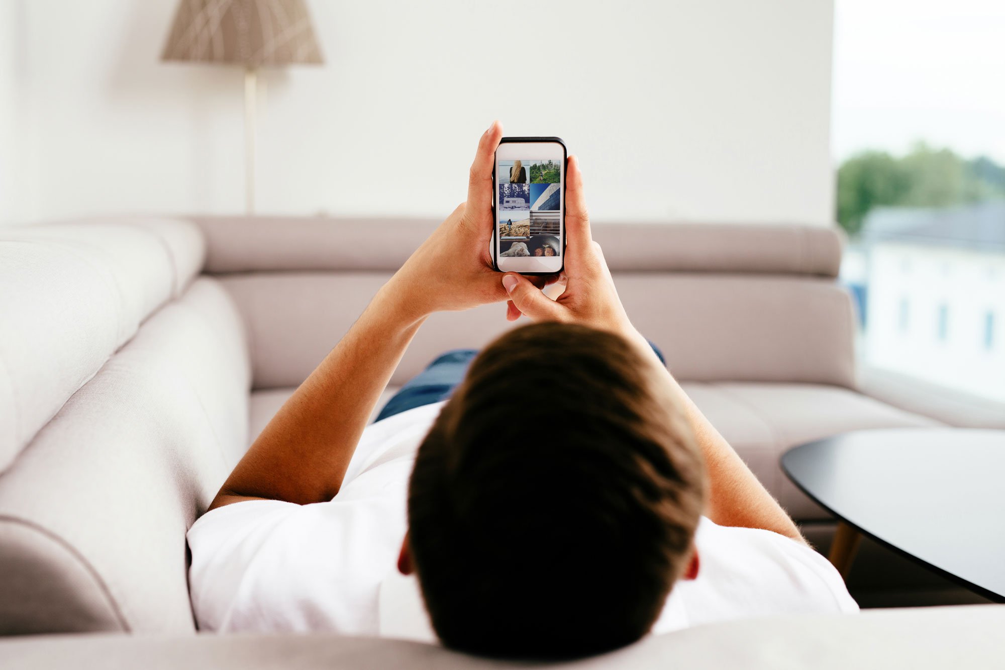 Man laying on couch with his feet up browsing internet on his phone