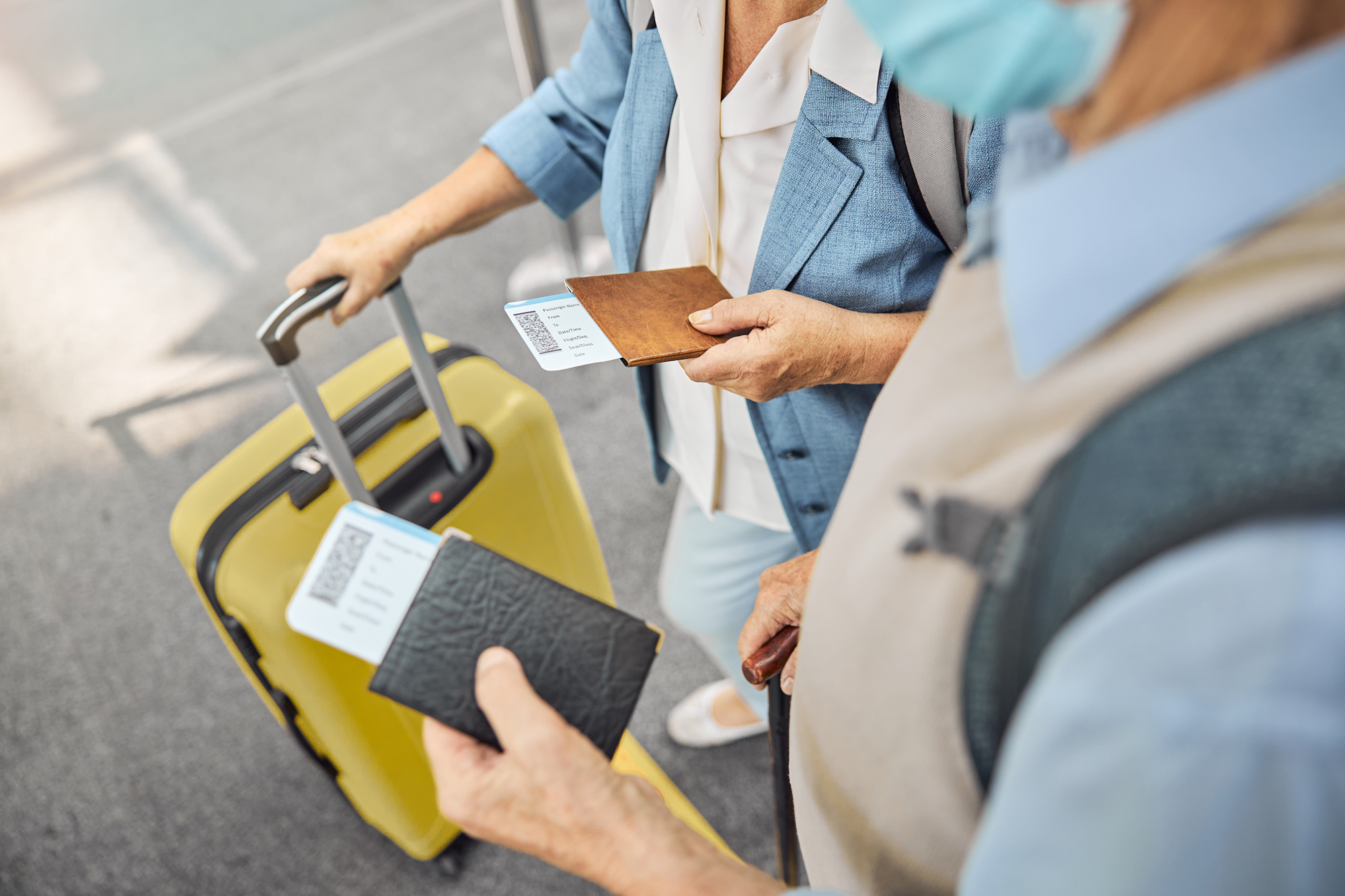 Close up of an older couple's hands holding passports and pulling luggage