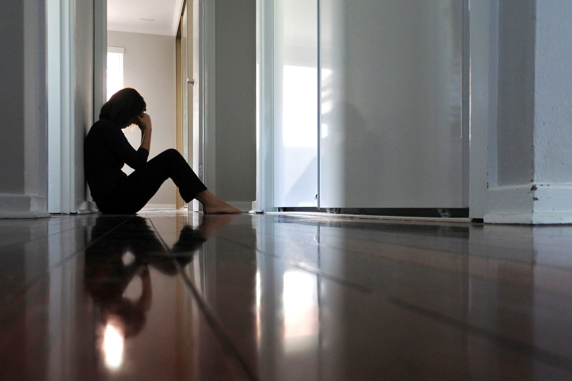 Sad woman sitting against wall in hallway with her head in her hands