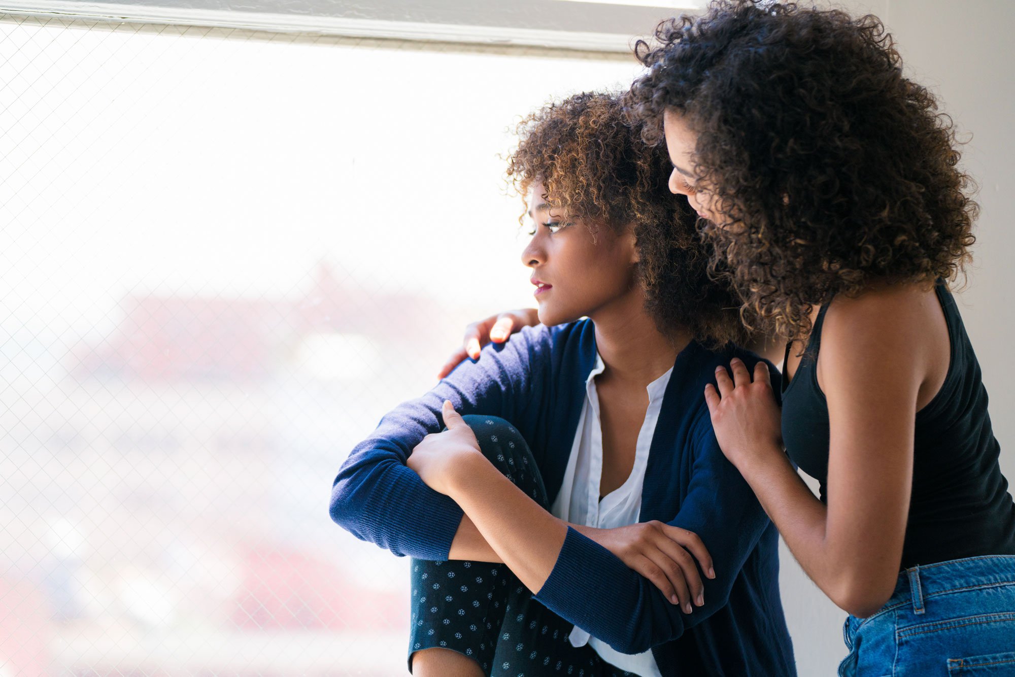 Woman hugging friend looking out window.