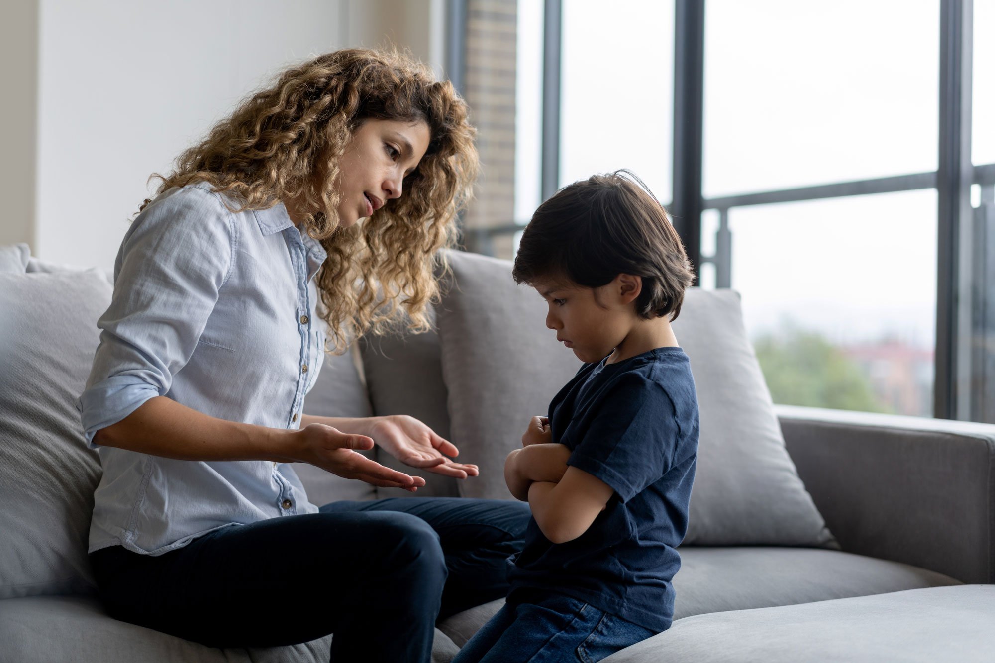 Mother talking to young son who is crossing his arms and frowning